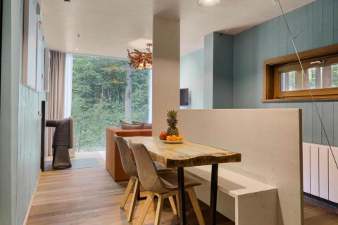 Dining area with wooden table, modern chairs, and bench seating inside The TreeLoft, forest view outside.