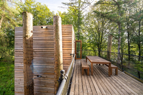 Terrazza di legno con tavolo e panche a The TreeLoft di YourNature, circondata da una foresta rigogliosa.