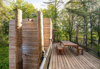 Terrazza di legno con tavolo e panche a The TreeLoft di YourNature, circondata da una foresta rigogliosa.