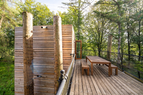 Treehouse outdoor deck with wooden table, benches, and modern design, surrounded by green forest scenery.