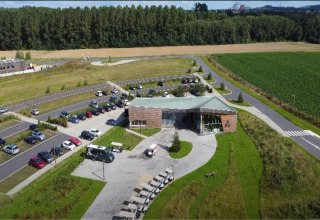 Luftfoto af The TreeLoft by YourNature i Belgien, omgivet af grønt landskab og parkering.