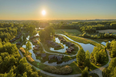 Glampinglocatie met huisjes aan kronkelend water, paden en bossen, vastgelegd bij zonsondergang.