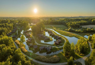 Glampinglocatie met huisjes aan kronkelend water, paden en bossen, vastgelegd bij zonsondergang.