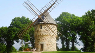 Casa de naturaleza molino de viento antiguo Gommenec'h, rodeada de árboles y césped bajo un cielo azul claro.