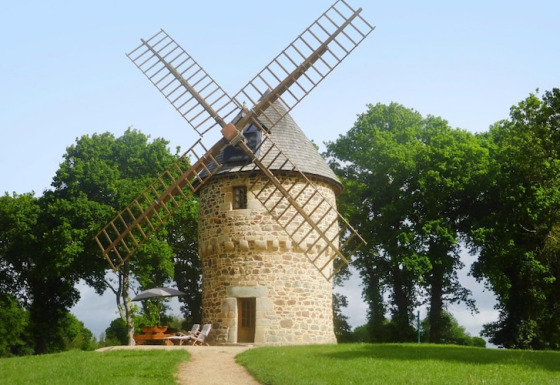 Ancient windmill Gommenec'h nature house, encircled by lush greenery, sitting under a clear blue sky.