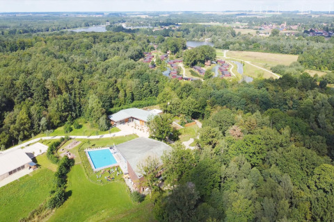 Aerial view of a glamping site featuring a swimming pool, forest cabins, water, and green landscapes.