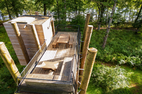 Treehouse The TreeLoft by YourNature, featuring a wooden deck with tables, surrounded by lush forest greenery.