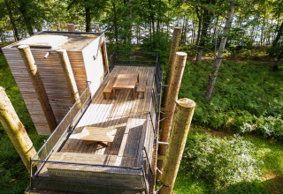 Casa del árbol The TreeLoft de YourNature, con terraza y mesas, rodeada de vegetación de bosque.