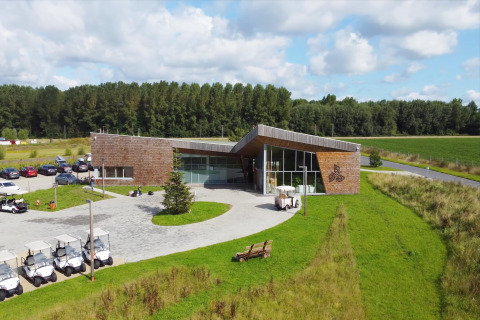 Glamping accommodation with a modern wood building, golf carts, parking, and lush green surroundings under sun.