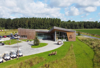 Glamping accommodation with a modern wood building, golf carts, parking, and lush green surroundings under sun.