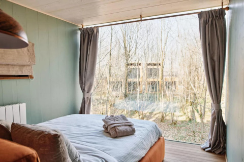 Dormitorio en The TreeLoft by YourNature en Bélgica, con gran ventana y vista al bosque exterior.