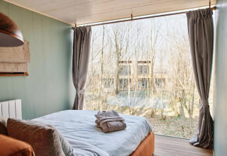 Dormitorio en The TreeLoft by YourNature en Bélgica, con gran ventana y vista al bosque exterior.