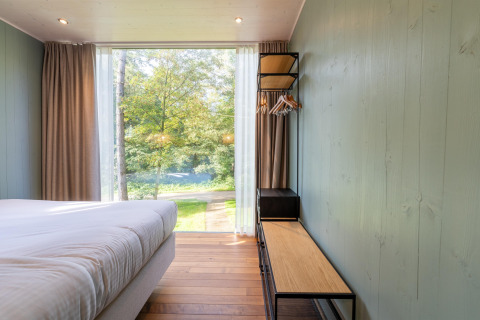 Dormitorio en The TreeLoft con gran ventana, cama, perchero abierto y vista al bosque exterior.