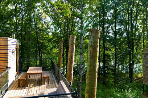 Terraza de madera con mesa y bancos en The TreeLoft, una casa del árbol rodeada de bosque en Bélgica.