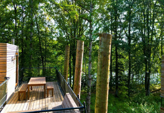 Terraza de madera con mesa y bancos en The TreeLoft, una casa del árbol rodeada de bosque en Bélgica.