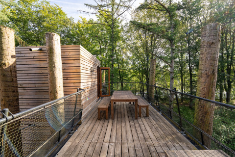 Terraza exterior de madera en The TreeLoft por YourNature, rodeada de árboles altos y diseño moderno.