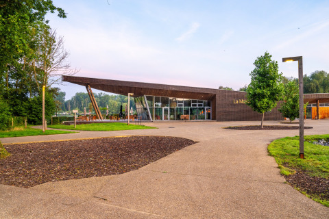 Contemporary wooden building at La Maison, surrounded by greenery and pathways, Belgium.