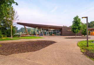 Contemporary wooden building at La Maison, surrounded by greenery and pathways, Belgium.