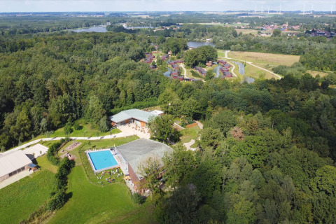 Aerial view of a glamping site featuring a swimming pool, forest area, and lodges surrounded by greenery.