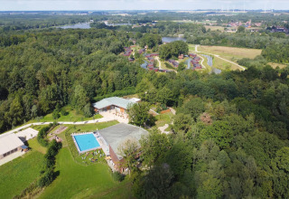 Aerial view of a glamping site featuring a swimming pool, forest area, and lodges surrounded by greenery.