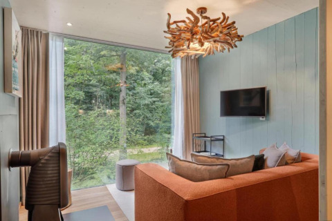 Modernes Wohnzimmer mit großer Fensterfront, orangefarbenem Sofa und Waldblick in The TreeLoft.