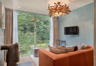 Modernes Wohnzimmer mit großer Fensterfront, orangefarbenem Sofa und Waldblick in The TreeLoft.
