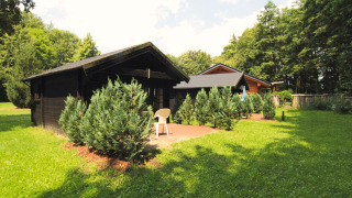 Twee houten blokhutten omgeven door groene struiken en gras bij Log cabin 30 m² onder blauwe hemel.