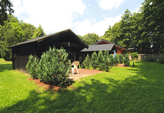 Dos cabañas de madera rodeadas de arbustos verdes y césped bajo cielo azul en Log cabin 30 m².