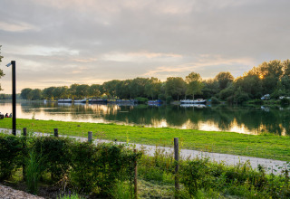 View of a calm river and boats with lush trees at sunset from a glamping accommodation in nature.