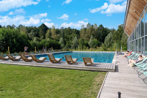 Piscina exterior en un alojamiento glamping rodeada de naturaleza, tumbonas y huéspedes relajándose.