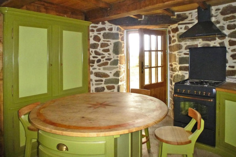 Cucina rustica in casa natura con mobili verdi, tavolo rotondo in legno e forno in antico mulino a vento, Francia