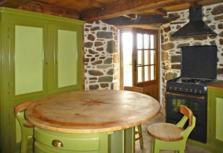 Cocina rústica en casa de naturaleza con armarios verdes, mesa redonda de madera y estufa en molino antiguo, Francia
