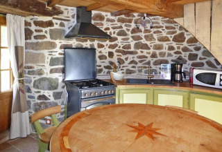 Cocina rústica en molino antiguo Gommenec'h, Francia, con paredes de piedra, estufa y mesa redonda.
