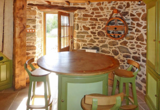 Cozy kitchen area in Ancient Windmill Gommenec'h, France, with stone walls, round wooden table and green chairs.