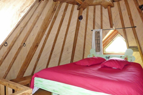 Dormitorio con paredes de madera inclinadas y ropa de cama roja en el antiguo molino de viento Gommenec'h, Francia.