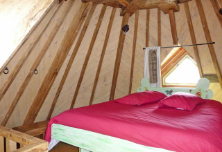 Bedroom with slanted wooden walls and red bedding in the ancient windmill house Gommenec'h, France.