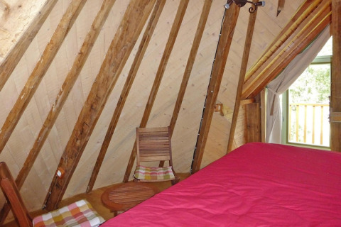 Interno di una stanza a Ancient windmill Gommenec'h, Francia, con travi in legno e copriletto rosso.