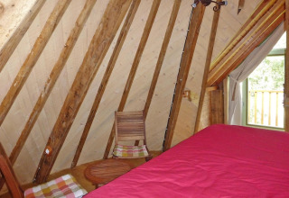 Interno di una stanza a Ancient windmill Gommenec'h, Francia, con travi in legno e copriletto rosso.