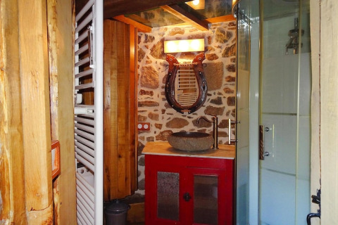 Rustic bathroom in Gommenec'h with stone wall, red vanity, stone basin, and lyre-shaped mirror.