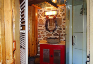 Rustic bathroom in Gommenec'h with stone wall, red vanity, stone basin, and lyre-shaped mirror.
