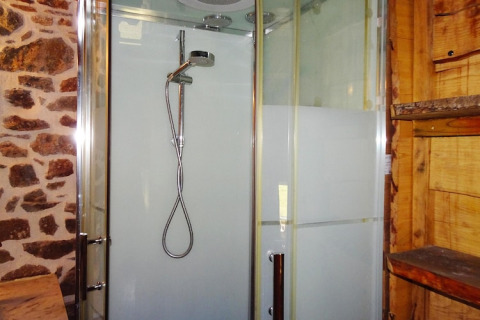 Modern shower cabin with glass doors and rustic stone and wood walls in a nature house in Gommenec'h, France.