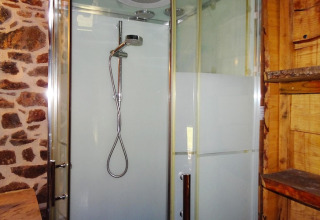 Cabina doccia moderna con porte in vetro e pareti in pietra e legno in una casa natura a Gommenec'h, Francia.