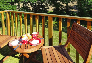 Wooden patio table with red cups and pastries, overlooking greenery at Ancient windmill Gommenec'h, France.
