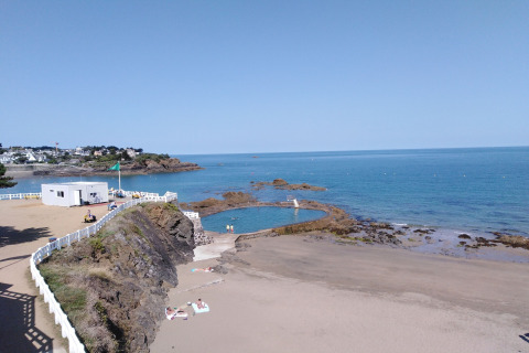Paesaggio costiero in Francia con spiaggia sabbiosa, piscina naturale, rocce e recinzione bianca.