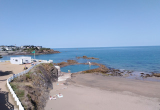 Paisaje costero en Francia con playa de arena, piscina natural, rocas y una cerca blanca junto al mar.