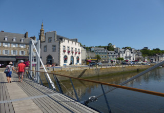 Coppia che passeggia su un ponte in legno vicino al fiume con hotel e case storiche a Gommenec’h, Francia.