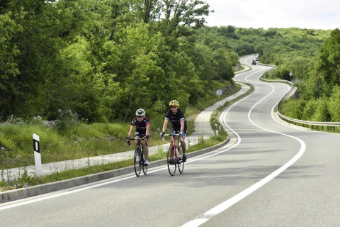 Twee fietsers rijden op een kronkelende weg omgeven door natuur bij Aminess Gaia Green Villas in Kroatië.