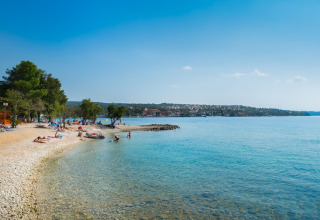 Prachtig strand en helderblauwe zee bij Aminess Gaia Green Villas Njivice, Kroatië, met badgasten.
