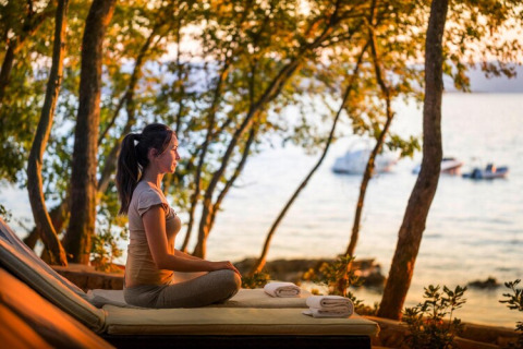 Vrouw mediteert bij zonsondergang aan zee bij Aminess Gaia Green Villas Njivice, Kroatië.