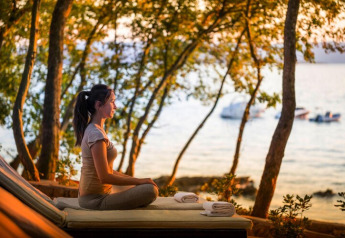 Kvinde mediterer ved solnedgang i naturen ved havet på Aminess Gaia Green Villas Njivice, Kroatien.